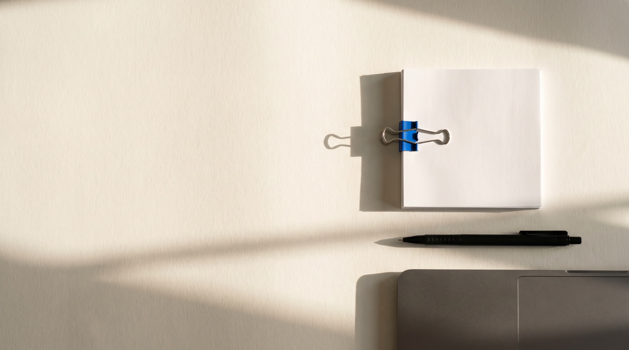 Pilha de papel branco presa por um prendedor azul sobre uma mesa clara